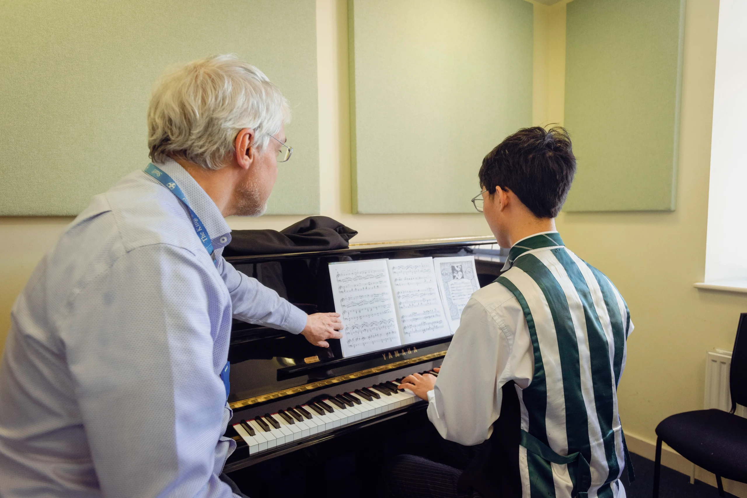 A teacher guiding a student through a music sheet while they play it on the piano at The King's Summer School's Music and Performance Academy